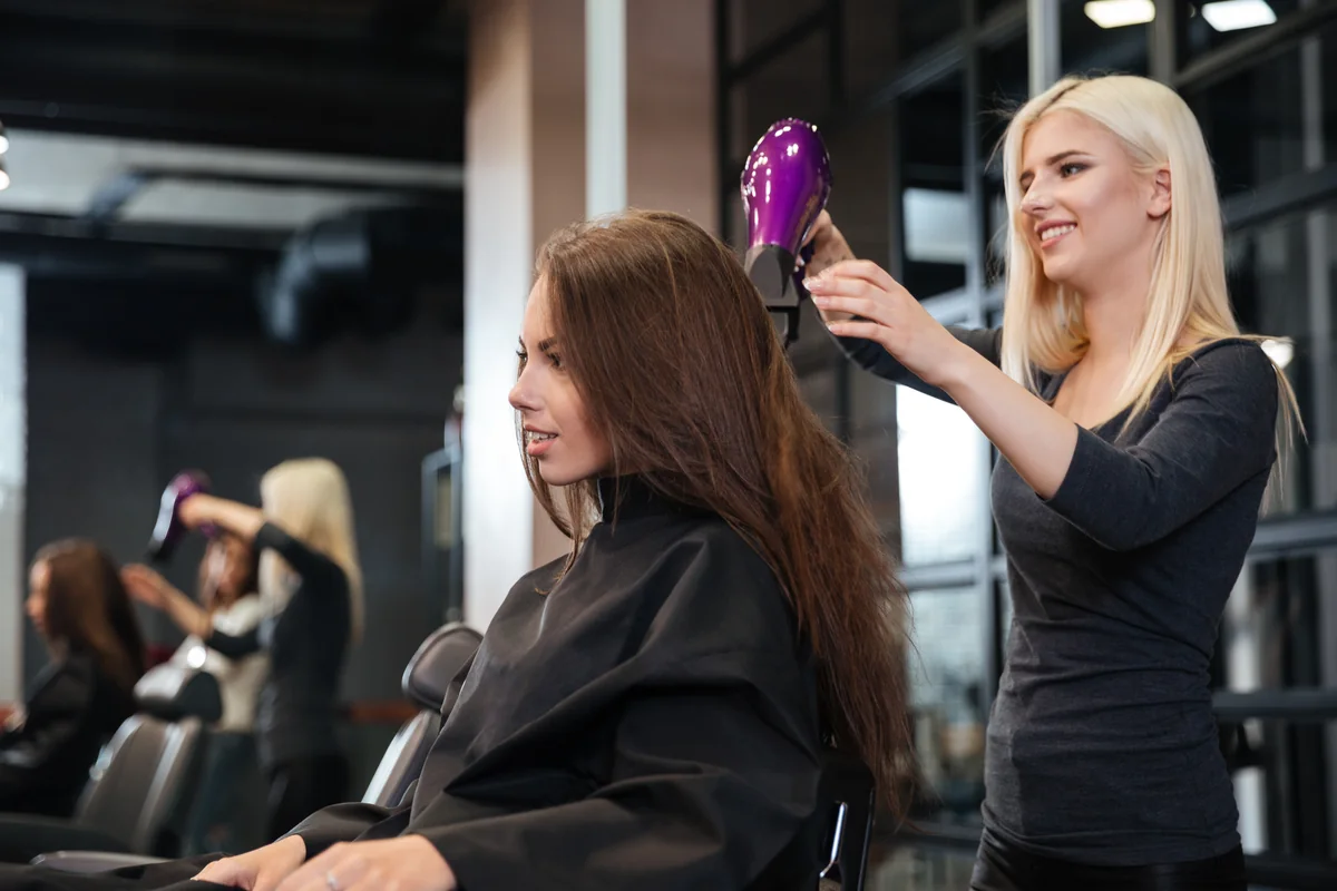 Stylistin föhnt die Haare einer Kundin